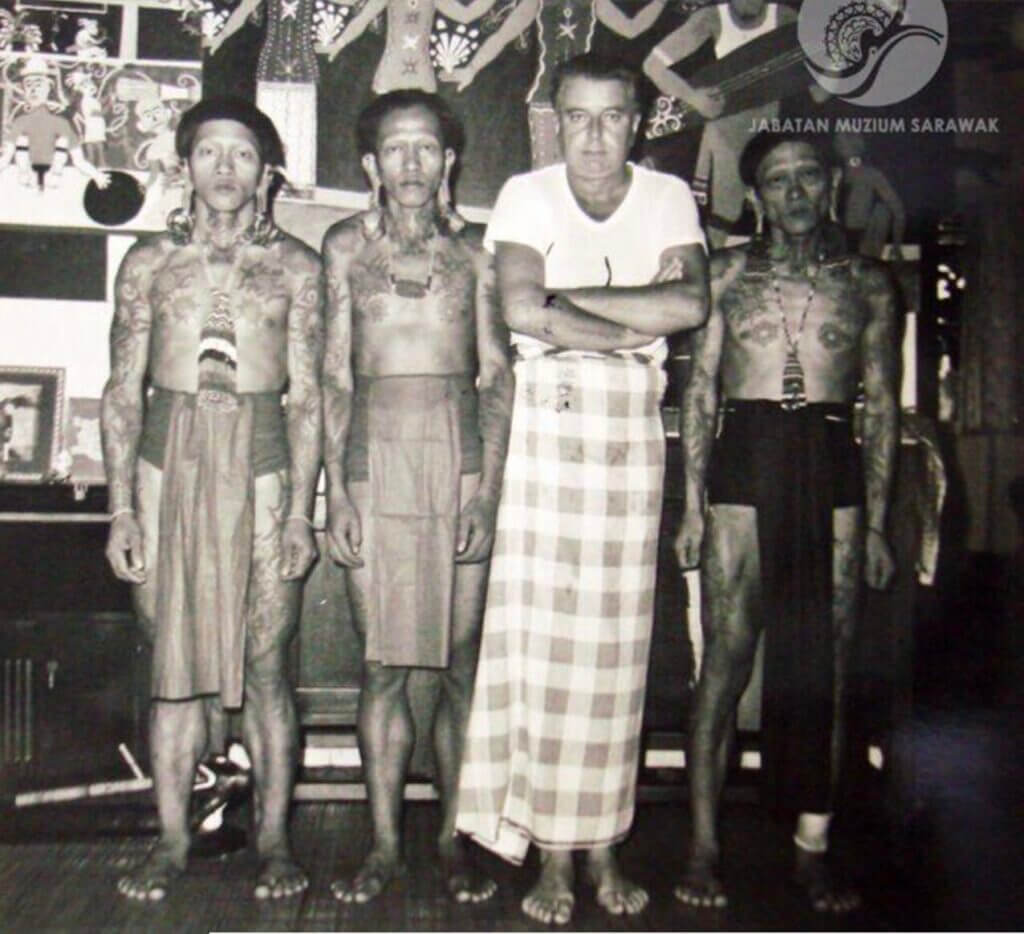 Tom Harnett Harrisson wrapped in checked blanket surrounded by Japanese indigenous men